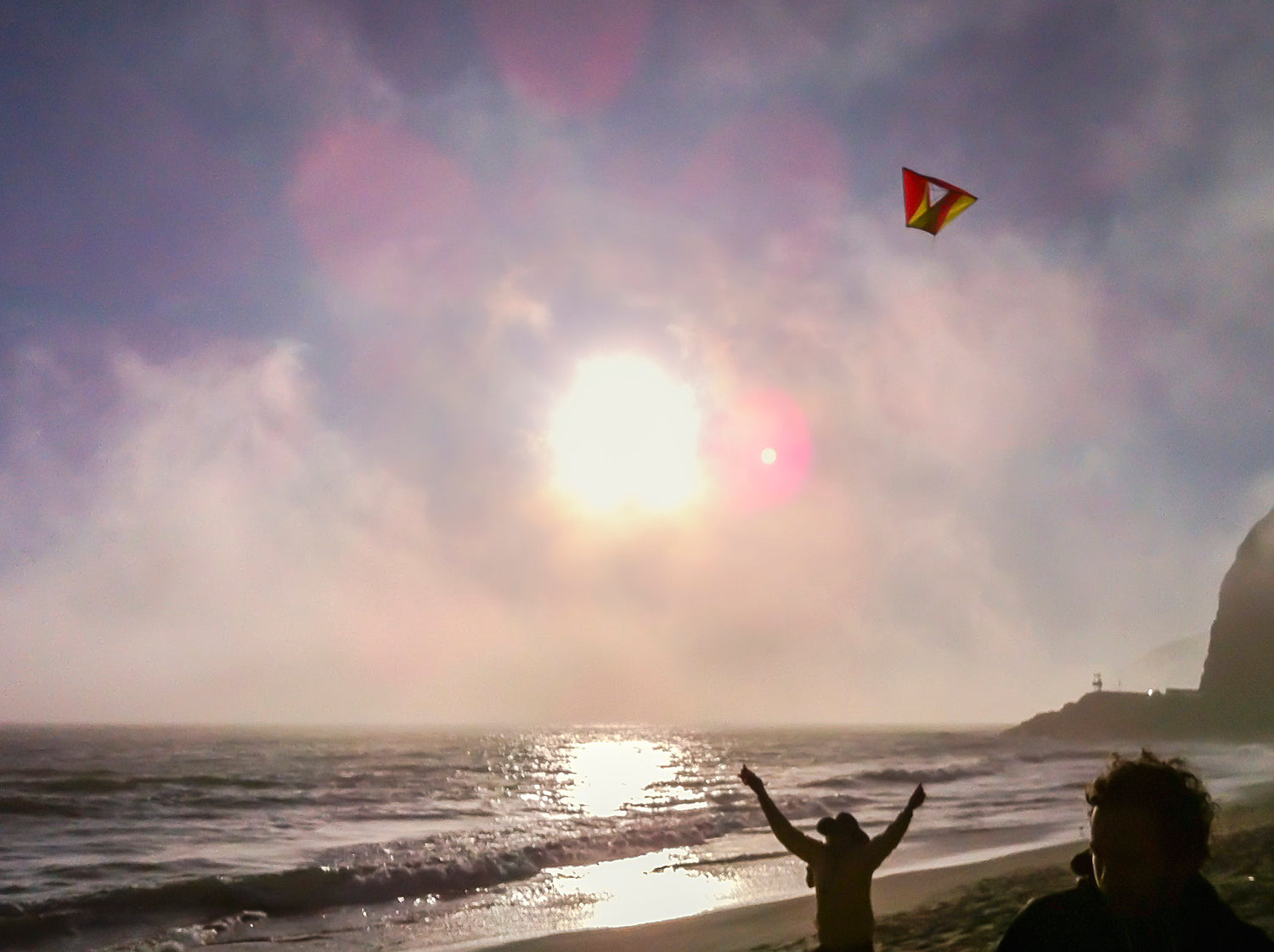 Person flying a kite on a beach with the Sun in the sky