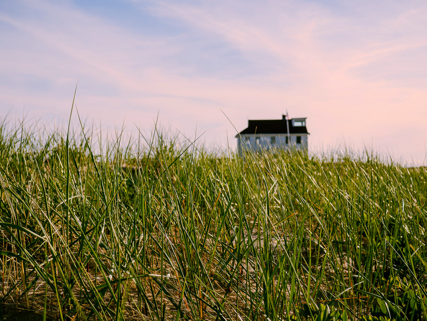 Small house on a grassy hill with a colorful sky