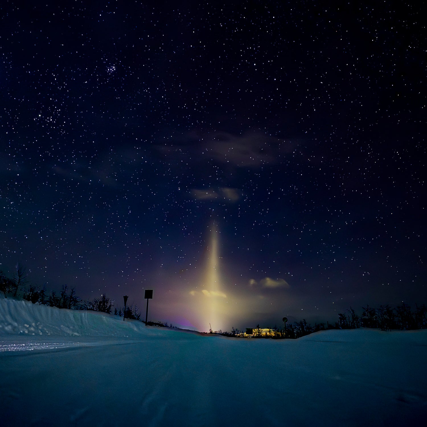 Starry night sky over a snowy landscape with a bright light source.